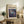 May include: Framed art print with "POLLOCK" text and cosmic blue abstract artwork featuring swirling galaxies and celestial orbs, displayed on rustic wooden console alongside fern plant, ceramic vase, and stacked books in modern living room setting with beige armchair