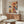 May include: Colorful abstract expressionist artwork with vibrant red, blue, yellow and black paint splatters and drips displayed above a mid-century modern walnut credenza in a minimalist living room. The large canvas features energetic brushstrokes and paint drips against a cream background. Room includes white upholstered chair, glass oval coffee table, and brass floor lamp.