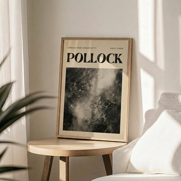 May include: Framed Jackson Pollock exhibition poster in light wood frame, featuring abstract black and white drip painting with "CHAOS AND CREATIVITY 1912-1956 POLLOCK" text, displayed on round wooden side table next to beige upholstered chair with plant shadows from window light on cream wall
