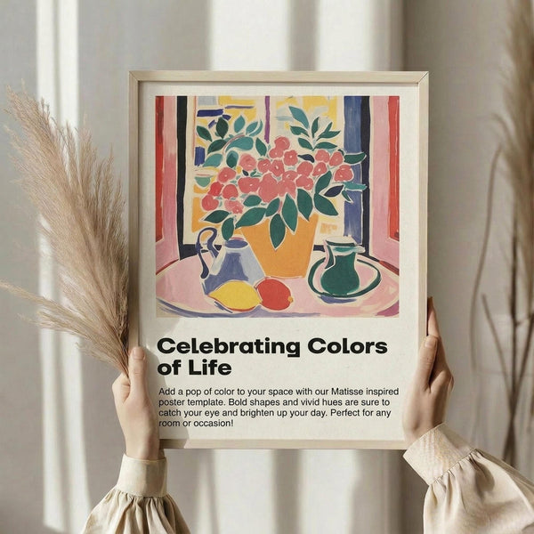 May include: Person holding framed colorful still life artwork in Matisse-inspired style, featuring orange vase with red flowers, blue and green pottery, yellow lemon and red apple on pink tablecloth. Light wood frame against neutral curtained background. Dried pampas grass visible on left side.