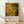 May include: Framed poster print featuring abstract art with organic yellow, green and gold flowing shapes and splatters in Jackson Pollock's distinctive drip painting style. The artwork shows cellular-like forms with black line divisions creating a mosaic pattern. Below the colorful abstract image is cream-colored text area with exhibition details. The wooden-framed print leans against a white wall on light wood flooring with soft natural lighting creating diagonal shadows across the scene.