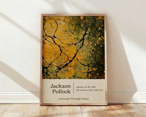 May include: Framed poster print featuring abstract art with organic yellow, green and gold flowing shapes and splatters in Jackson Pollock's distinctive drip painting style. The artwork shows cellular-like forms with black line divisions creating a mosaic pattern. Below the colorful abstract image is cream-colored text area with exhibition details. The wooden-framed print leans against a white wall on light wood flooring with soft natural lighting creating diagonal shadows across the scene.
