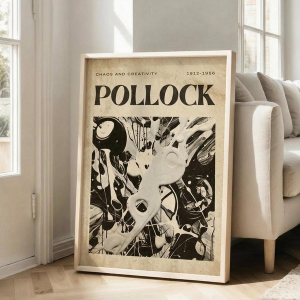 May include: Large framed abstract art print leaning against white wall next to beige upholstered chair in bright living room. Poster features bold black and white paint splatters and drips in energetic composition with "POLLOCK" text at top and "CHAOS AND CREATIVITY 1912-1956" subtitle. Natural wood frame, aged beige background texture, sunlight streaming through windows onto hardwood floors.