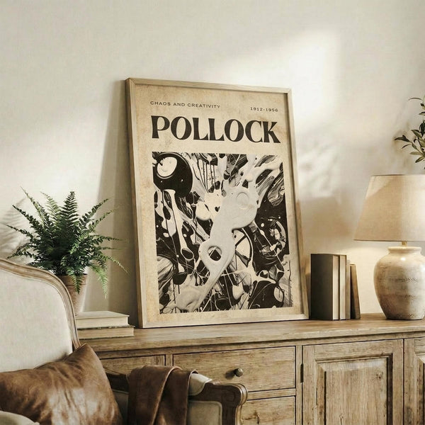 May include: Framed vintage-style art poster featuring abstract black and white Jackson Pollock painting with chaotic drip patterns and organic forms, displayed on rustic wooden sideboard alongside fern plant, ceramic vase, and books in warm neutral living room setting with beige armchair