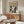 May include: Black and white Jackson Pollock art poster hanging above a mid-century modern walnut credenza in a minimalist living room. The vintage-style poster features abstract drip painting artwork with "POLLOCK" and "CHAOS AND CREATIVITY 1912-1956" text. Room has cream walls, white curved chair, oval glass coffee table, and warm wood furniture with clean lines.