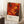 May include: Framed abstract art poster with vibrant red, orange, and yellow swirling patterns and black splatters, featuring Jackson Pollock exhibition text at bottom. Poster leans against white wall corner on white textured rug, next to wooden side table with coffee cup and saucer, with beige throw blanket visible on right side.