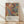 May include: Framed Jackson Pollock exhibition poster leaning against white textured wall on light wood floor. Abstract artwork features energetic splashes and drips in orange, blue, yellow, and black paint. Poster has cream bottom section with black text reading artist name, exhibition dates January 10-20, 1956, 8th Avenue New York City location, and "A Journey Through Chaos" subtitle. Natural wood frame surrounds the print. Soft shadows cast across the minimal room setting.
