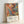 May include: Framed abstract expressionist art print with vibrant splashes and drips of orange, blue, yellow, and black paint in chaotic swirls and lines. The poster features exhibition text reading "Jackson Pollock January 10-20, 1956 8th Avenue, New York City A Journey Through Chaos" below the colorful artwork. Light wood frame leans against white wall, showing the energetic paint-splatter style characteristic of action painting.
