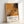 May include: Framed abstract art poster in light wood frame leaning against white wall. Features orange and black paint splatters and drips in Jackson Pollock's signature drip painting style. White bottom section displays artist name, exhibition dates "January 10-20, 1956", location "8th Avenue, New York City", and subtitle "A Journey Through Chaos". Modern museum exhibition poster design with clean typography.