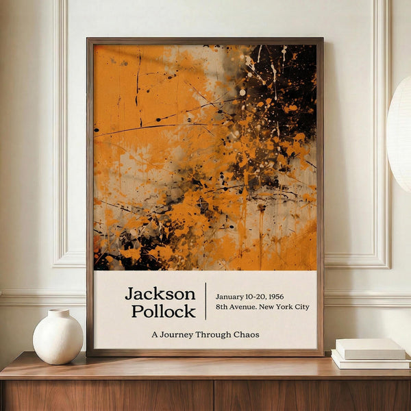 May include: Abstract expressionist style poster featuring orange, black, and beige paint splatters and drips with exhibition text below. The framed artwork sits on a wooden sideboard beside a white ceramic vase and books in an elegant room with cream walls and white molding. The composition shows dynamic paint strokes and scattered dots creating an energetic, chaotic pattern.