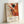 May include: Framed abstract art poster featuring Jackson Pollock's dynamic paint splatters in orange, red, black, yellow and green against cream background. Exhibition details show January 10-20, 1956, 8th Avenue, New York City with "A Journey Through Chaos" subtitle. Light wood frame leans against white wall, casting subtle shadow.