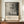 May include: A framed exhibition poster featuring Jackson Pollock's abstract black and white paint splatters and drips on cream background, displayed on a wooden sideboard beside a white ceramic vase and stacked books in an elegant room with cream walls and crown molding.