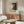 May include: Jackson Pollock exhibition poster displayed in modern living room with warm wood sideboard, white sculptural chair, glass coffee table, and copper floor lamp. The vintage-style poster features abstract black and white artwork with bold typography advertising dates in 2030. Soft natural lighting creates shadows across polished floors in minimalist interior setting.