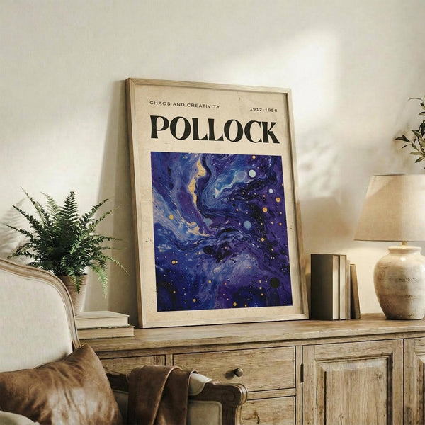 May include: Framed poster with cream background featuring "POLLOCK" text and "CHAOS AND CREATIVITY 1912-1956" header above swirling blue and purple abstract artwork with gold dots, displayed on rustic wooden sideboard alongside fern plant, ceramic vases, books, and brown leather chair in neutral-toned living room setting.