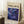 May include: Framed art print with cream background featuring "POLLOCK" text and "CHAOS AND CREATIVITY 1912-1956" above swirling blue and purple abstract design with golden dots, leaning against white wall corner next to coffee cup on wooden block and beige textured fabric on white rug