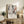 May include: Abstract art poster with black, white, and orange paint splatters in wooden frame, displayed on rustic wood sideboard next to fern plant, books, ceramic vase, and beige armchair in modern living room setting with warm natural lighting