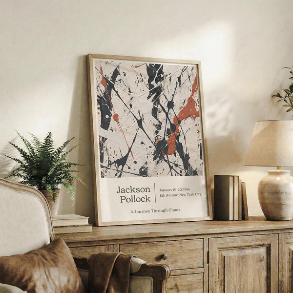 May include: Abstract art poster with black, white, and orange paint splatters in wooden frame, displayed on rustic wood sideboard next to fern plant, books, ceramic vase, and beige armchair in modern living room setting with warm natural lighting