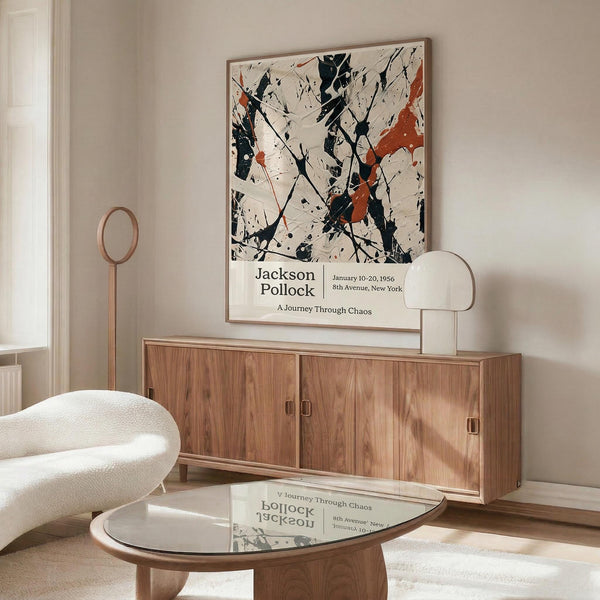 a modern living room with a large abstract painting hanging on the wall above a wooden cabinet. The painting has a mix of black, white, and orange colors, creating a striking visual contrast. The room also includes a white sofa, a round glass coffee table, and a lamp on a side table.