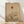 May include: Minimalist Japanese-inspired artwork in light wood frame leaning against white wall on blonde hardwood floor. Beige textured background features geometric composition with orange-red sun, curved lines, rolling hills in earth tones, and delicate bare tree with spreading branches. Soft natural lighting creates diagonal shadows across the scene.
