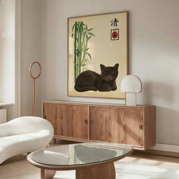 May include: Dark tabby cat resting in front of framed Asian-inspired artwork featuring green bamboo stalks and Japanese characters on cream background. Modern living room setting with walnut sideboard, white mushroom table lamp, cream curved chair, glass coffee table, and wooden floor lamp. Minimalist decor with natural wood tones and soft lighting.