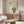 May include: A framed poster featuring a cute black cat with large yellow eyes sitting next to green bamboo, with Japanese characters above, displayed on a walnut wood credenza in a modern living room with cream walls, white sculptural chair, glass coffee table, and white table lamp