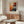 May include: Framed Jackson Pollock abstract expressionist art print hanging above wooden sideboard in modern living room. Colorful splattered paint design features vibrant oranges, reds, blues, and black against cream background. Room shows white curved chair, glass oval coffee table, floor lamp, and white walls with natural lighting.