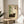 May include: Framed poster displayed on wooden round side table next to beige upholstered chair in sunlit room. Artwork features dark tabby cat resting beside green bamboo stalks on cream background with Japanese characters and small red rectangular element. Natural wood frame complements modern minimalist decor with plant shadows visible on white wall.
