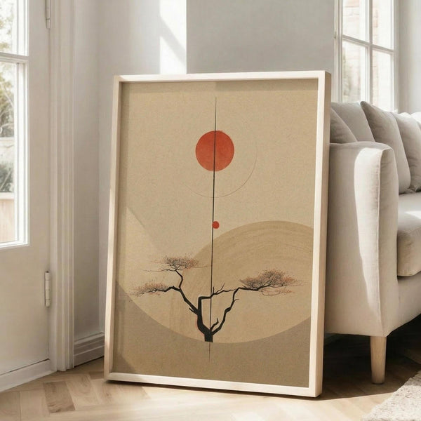 May include: Minimalist Japanese-inspired art print in light wood frame leaning against white wall beside beige upholstered chair. Artwork features warm beige background with red-orange sun, curved lines, silhouetted bare tree, and large tan circle. Natural lighting from tall windows creates soft shadows on hardwood floor.