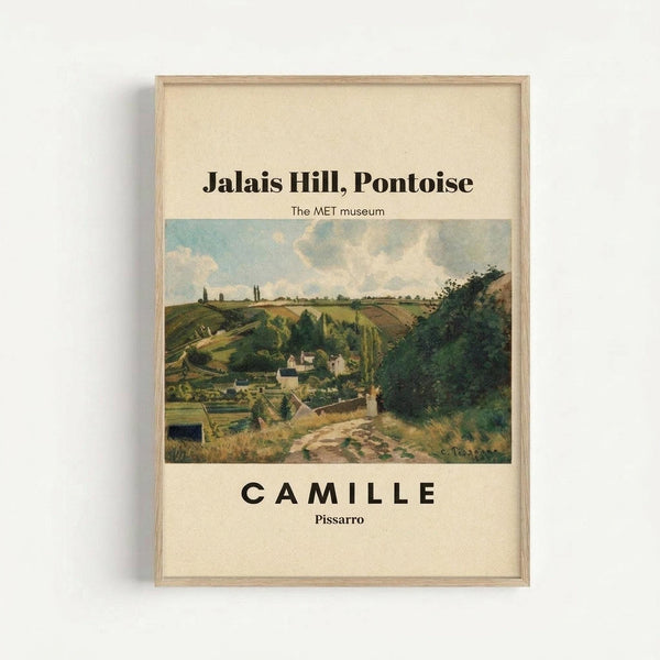 May include: Framed art print featuring a pastoral landscape painting with rolling green hills, a winding dirt path, small village buildings nestled in a valley, and cloudy blue sky. The artwork shows Impressionist-style brushwork in earth tones of green, brown, and blue. Text reads "Jalais Hill, Pontoise" at top, "The MET museum" below, and "CAMILLE Pissarro" at bottom on cream background. Displayed in light wood frame against white wall.