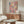 May include: Abstract splatter painting with vibrant pink, blue, yellow and purple paint drips and splatters on white background, displayed above wooden sideboard in modern living room with white curved chair, glass coffee table, and minimalist decor