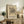 May include: Framed abstract art print featuring black geometric lines, circles, and organic shapes on beige background, displayed on rustic wooden sideboard alongside fern plant, ceramic vase, and books in neutral-toned living room with cream upholstered furniture and soft natural lighting.