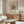 May include: A framed vintage-style poster featuring Wassily Kandinsky's abstract geometric artwork in black lines and curves on cream background, displayed above a mid-century modern wooden credenza with sliding doors. The room shows a white curved lounge chair, glass oval coffee table, modern brass floor lamp, and small white table lamp, creating a minimalist Scandinavian-inspired interior with neutral tones and natural lighting.