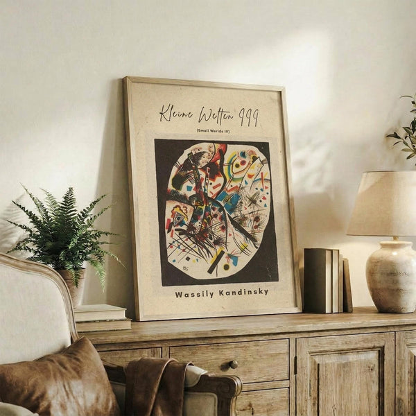 May include: Framed abstract art print featuring colorful geometric shapes and lines in circular composition on cream background, displayed on rustic wooden sideboard with fern plant, ceramic vase, and stacked books in neutral-toned living room setting with beige upholstered furniture