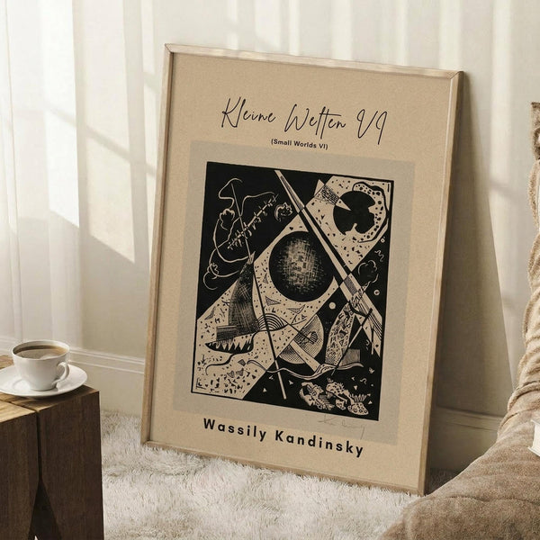 May include: Abstract geometric artwork print in warm beige mat and light wood frame, leaning against white wall corner. Black and white modernist design features angular shapes, celestial elements, and intricate patterns. Artist name "Wassily Kandinsky" printed below image. Small wooden side table with white coffee cup visible on left. Cream textured rug and neutral bedding create cozy room setting with natural window lighting.