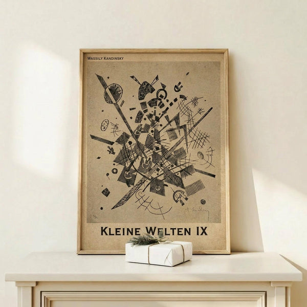 May include: Framed abstract art print by Wassily Kandinsky featuring geometric black line drawings on beige background, displayed on light wood console table with small white wrapped gift beside it against cream wall