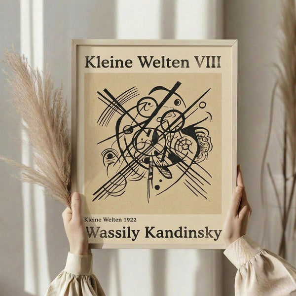 May include: Framed abstract art print featuring black geometric lines, circles, and organic shapes on cream background, held by person in beige clothing with dried wheat stalks, against white curtained window in neutral-toned room setting.