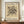 May include: Framed abstract art print with black geometric lines, circles, and curved forms on cream background, displayed on wooden sideboard next to white ceramic vase and stacked books in room with beige walls and white trim molding.