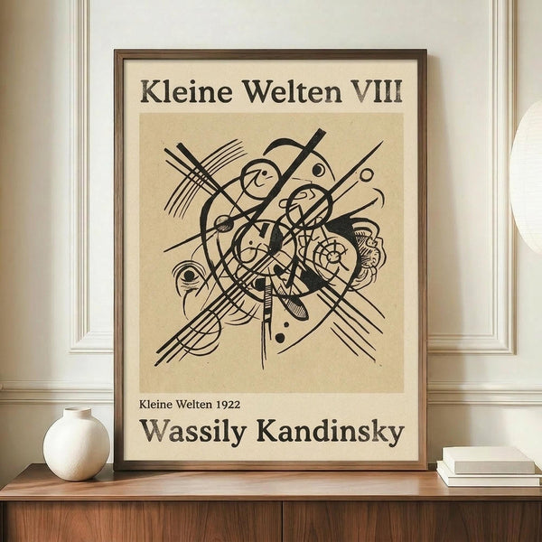 May include: Framed abstract art print with black geometric lines, circles, and curved forms on cream background, displayed on wooden sideboard next to white ceramic vase and stacked books in room with beige walls and white trim molding.