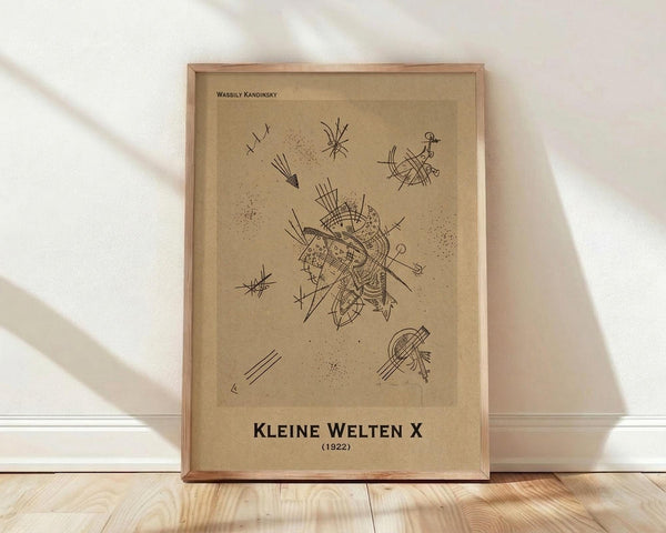 May include: Framed abstract art print in light wood frame leaning against white wall on wooden floor. Features geometric black line drawings on tan background with artist name at top and German title with date at bottom. Soft natural lighting creates diagonal shadows across white textured wall.