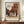 May include: Framed art print of a Dutch Golden Age street scene with red brick buildings, cobblestone courtyard, and small figures in period clothing under a cloudy sky. The poster is displayed on a wooden sideboard next to a white ceramic vase and stacked books in a neutral-toned room with white paneled walls.