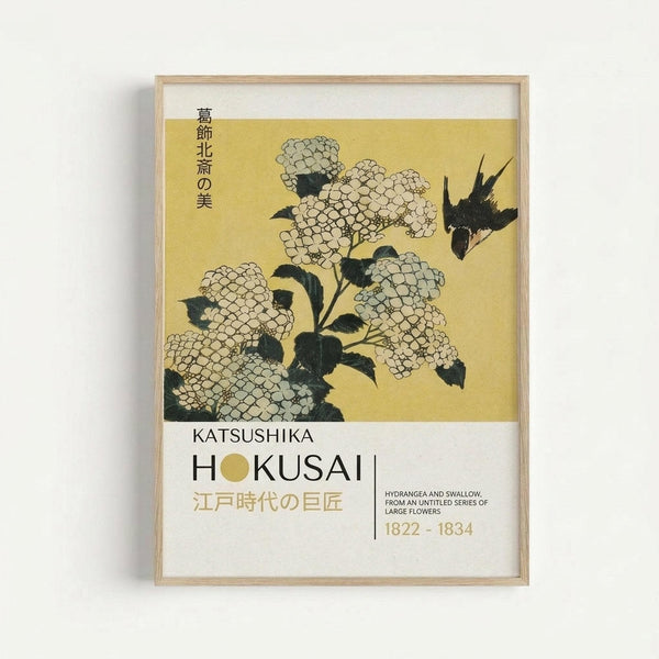 May include: Framed Japanese woodblock print poster showing white hydrangea flowers with dark green leaves and a black swallow against golden yellow background. Features Japanese text at top and museum-style typography below reading "Katsushika Hokusai" with artwork details. Light wood frame against white wall.