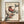 May include: Framed vintage Japanese woodblock print featuring two birds with long curved beaks and reddish-brown plumage perched on dark branches against cream background. The artwork displays traditional ukiyo-e style with muted earth tones. Frame sits on wooden credenza beside white ceramic vase and stacked books in elegant room with white paneled walls.