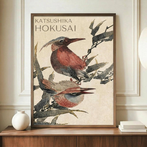 May include: Framed vintage Japanese woodblock print featuring two birds with long curved beaks and reddish-brown plumage perched on dark branches against cream background. The artwork displays traditional ukiyo-e style with muted earth tones. Frame sits on wooden credenza beside white ceramic vase and stacked books in elegant room with white paneled walls.