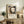 May include: Framed Japanese woodblock print featuring a ghostly female figure with long black hair and pale white face, displayed on a rustic wooden credenza alongside fern plant, books, and ceramic vase in warm-toned living room setting with beige upholstered furniture