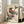 May include: Framed art print featuring two colorful birds perched on leafy branches in traditional Japanese woodblock style, displayed against white wall next to beige upholstered chair in bright living room with large windows and hardwood floors. The birds show rich reddish-brown plumage with detailed feather textures on cream background.
