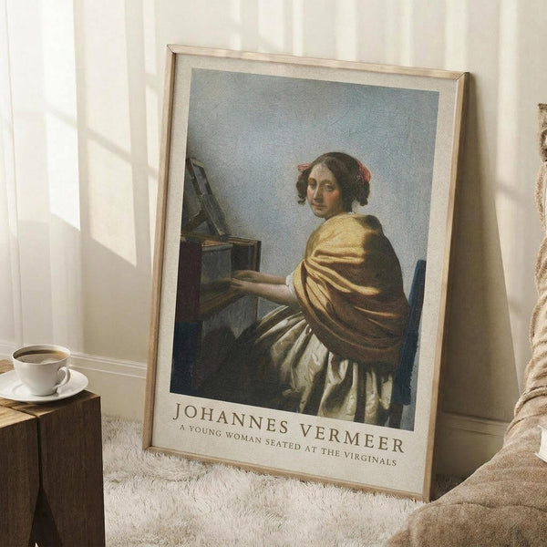 May include: Framed art print of Vermeer's classical painting showing a young woman in yellow and white robes seated at a virginals keyboard instrument, displayed on white textured rug against bright white wall with window light, alongside wooden side table with coffee cup and beige throw blanket.