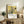 May include: Framed poster featuring Japanese artwork of white hydrangea flowers with dark green leaves against yellow background, displayed on rustic wooden sideboard. Room setting shows fern plant, ceramic vases, books, and cream-colored furniture. Poster has museum-style text layout with artist name and dates below floral illustration.