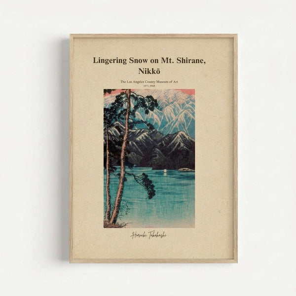 A framed vintage Japanese woodblock print depicting a serene lake scene with snow-capped mountains in the background. The artwork shows tall pine trees in the foreground, their dark silhouettes contrasting against turquoise and blue water. The composition features delicate line work characteristic of traditional Japanese art, with subtle color gradations from coral pink sky to deep teal water. The print is matted in cream-colored paper within a light wooden frame, displaying museum attribution t