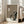 May include: Framed poster print featuring a stylized black cat with large white eyes and pointed ears sitting beneath a white paper lantern with floral details, with Japanese characters above. The artwork has a textured beige and cream background with a cracked vintage appearance. The wooden frame leans against a light gray wall next to a beige upholstered sofa in a bright, minimalist living room with white window trim and natural lighting.