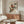 May include: Japanese-style bird print displayed above wooden sideboard in modern living room. Two colorful birds with reddish-brown and blue plumage perch on leafy branches against cream background. Framed artwork positioned over mid-century walnut credenza with sliding doors. White sculptural chair and glass coffee table with wood base visible. Minimalist spherical table lamp and floor lamp complete the scene.
